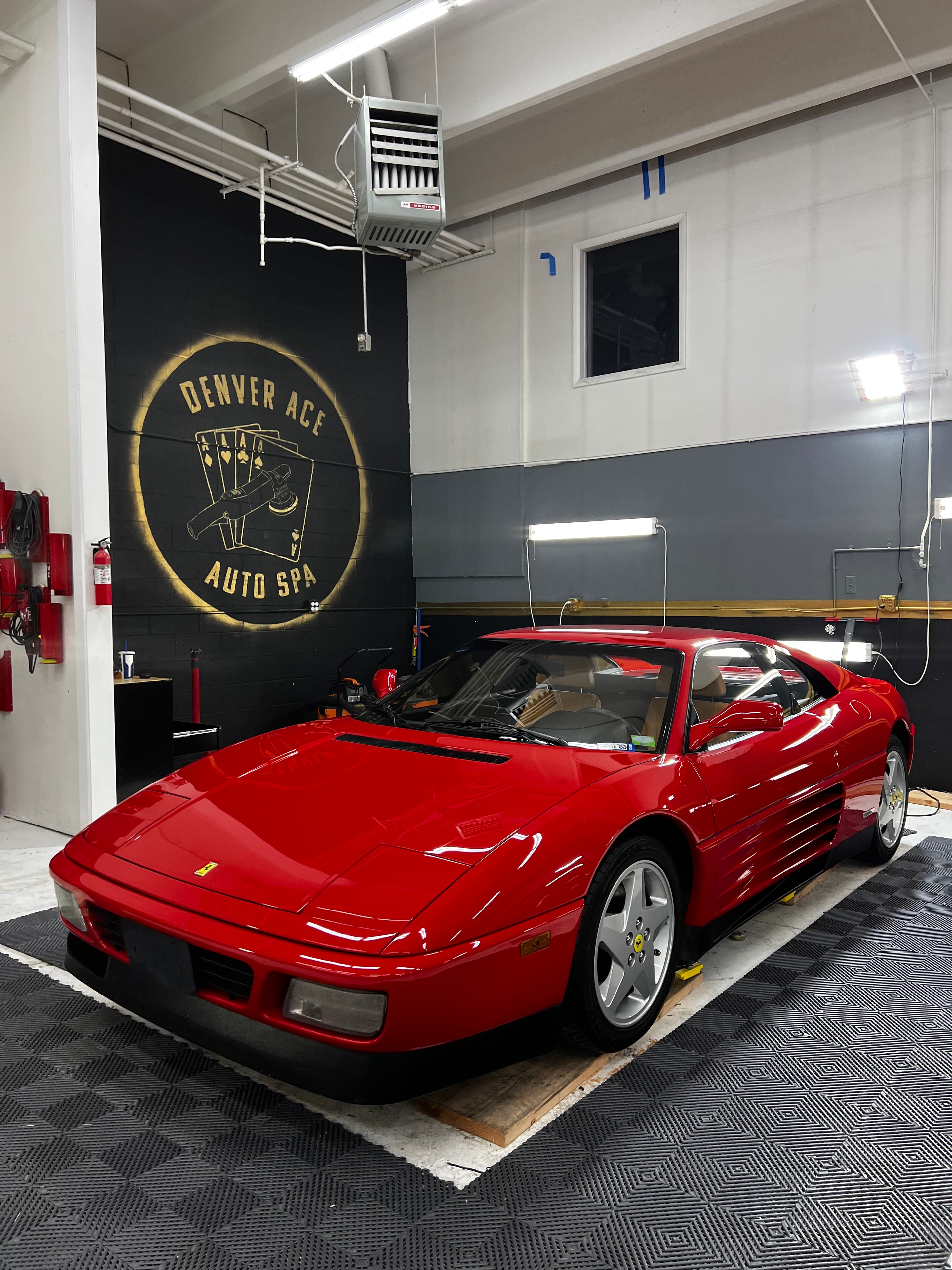 Red Ferrari 348 in the Denver Ace Auto Spa shop bay with the branded wall mural visible