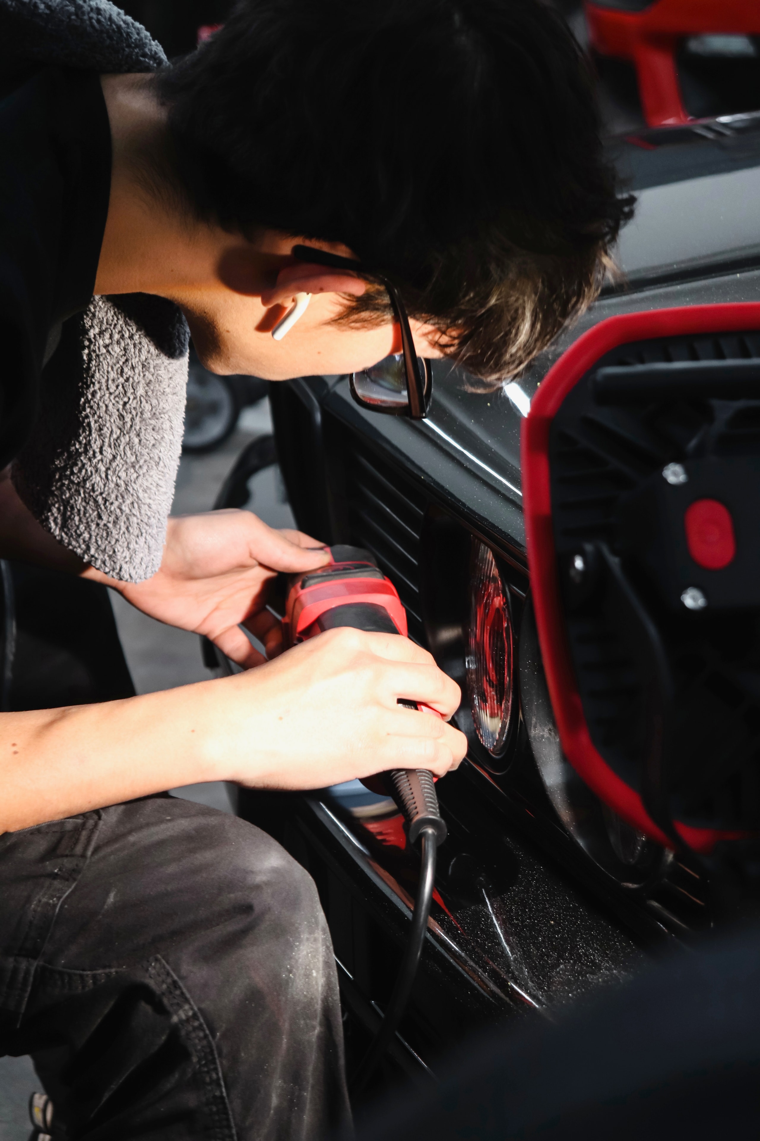 Technician machine-polishing the paint near the tail lights of a black vehicle