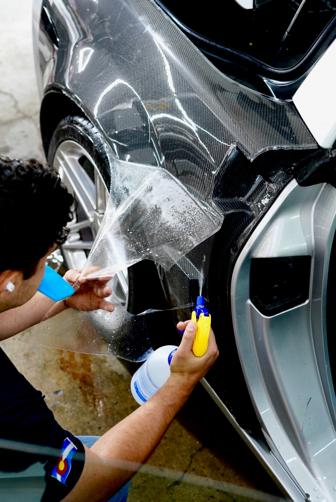 Technician applying and smoothing paint protection film on a vehicle bumper with spray bottle