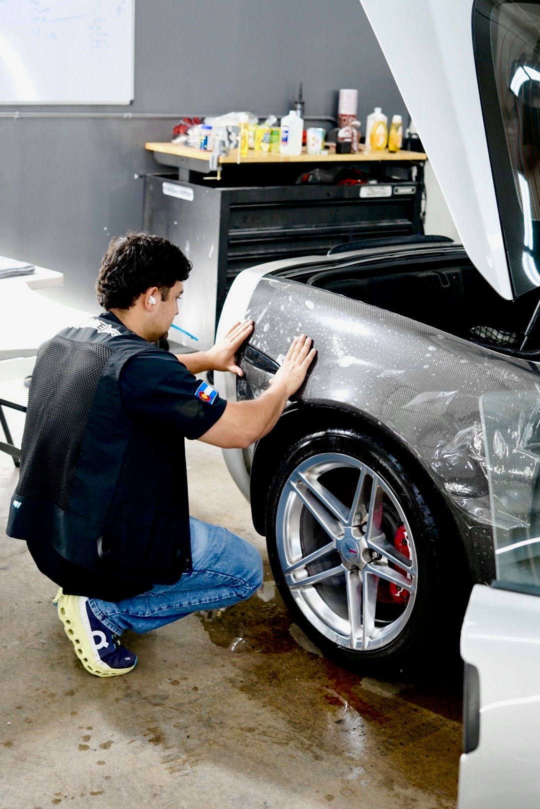 Technician pressing paint protection film onto a carbon fiber bumper panel